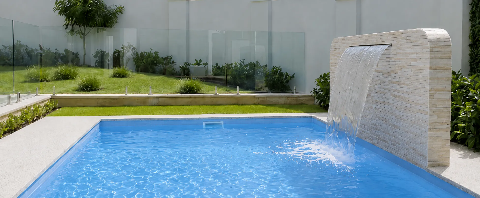 Bermuda Blue Sparkle fibreglass pool with a curved stone water feature in a modern landscaped backyard